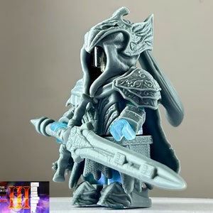 Puede incluir: Una figura en miniatura de un caballero impresa en 3D en gris, que lleva un casco y una armadura detallados, sosteniendo una espada. La figura está en posición de pie con la espada en posición defensiva.