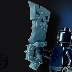 May include: A gray plastic miniature sword with a skull-like design and a spiked handle. The sword is held by a black miniature figure.