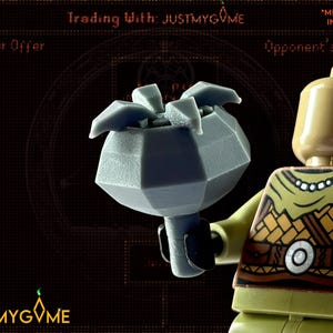 May include: A gray, geometric Lego accessory held by a Lego figure. The accessory has a flower-like top. The figure has a tan head and green and brown torso. The background is dark with text that reads "Trading With: JUSTMYGVME".