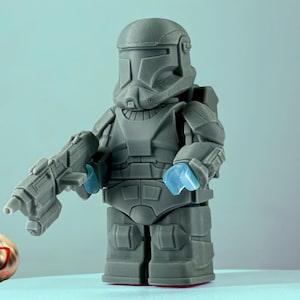 May include: A gray and black action figure of a Star Wars clone trooper with a blue blaster rifle. The figure is wearing a helmet and armor.