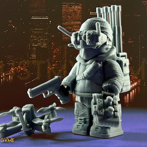 May include: A grey figurine of a character in tactical gear, holding a pistol and standing next to a drone. The figure wears a beanie, goggles, and a backpack. The background shows a cityscape with the text "JUSTMYGVME".