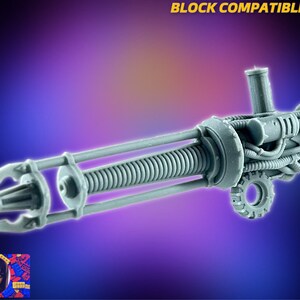 Op de afbeelding: Een grijs plastic model van een futuristisch wapen met een veermechanisme, pijpen en een wiel. Het wapen is gelabeld met "BLOCK COMPATIBLE".
