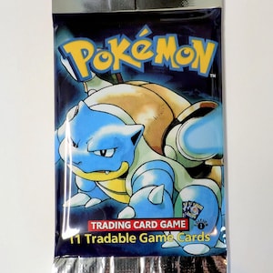 May include: Sealed Pok&eacute;mon Trading Card Game pack featuring Blastoise. The packaging is dark blue with the Pok&eacute;mon logo and a Blastoise illustration. The pack includes 11 tradable game cards.