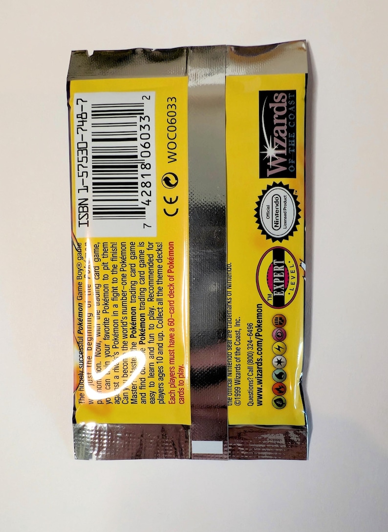 May include: Sealed Pok&eacute;mon trading card game pack with yellow and silver packaging. Features the Wizards of the Coast logo, Nintendo seal, and text including "Expert Level". The pack includes the ISBN 1-57530-748-7.