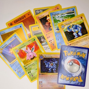 May include: A collection of Pok&eacute;mon trading cards featuring various characters and energy cards. The cards have yellow borders and feature colorful illustrations of Pok&eacute;mon like Machamp, Magikarp, and Starmie. The backs of the cards have a blue and white Pok&eacute; Ball design.