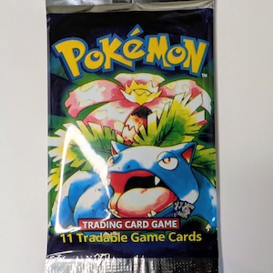 May include: Sealed Pok&eacute;mon trading card game pack. The pack features a blue and green background with the Pok&eacute;mon logo in yellow. The image on the pack shows a blue and red Pok&eacute;mon with a flower. The text reads "11 Tradable Game Cards."