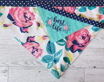 May include: A white bandana with a floral pattern featuring pink roses and green leaves. The bandana has a turquoise blue layer on top with the text "best life" embroidered in white.