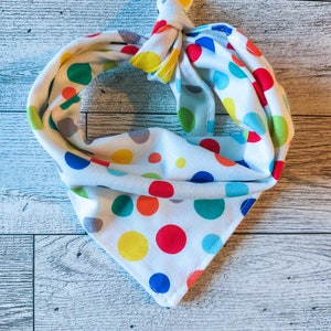 May include: A white bandana with colorful polka dots. The bandana is tied in a knot at the top and the ends are hanging down.