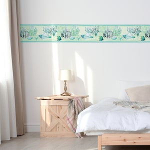 May include: A white bedroom with a wooden nightstand and a white bed with a white blanket and a beige pillow. The wall has a light blue and green wallpaper border with a seashell and coral design.
