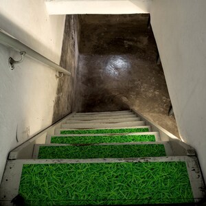 May include: A set of stairs leading down to a basement. The stairs are painted white and have green grass-like treads.
