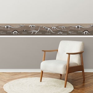 May include: A brown wall with a white dinosaur skeleton border. The border features various dinosaurs, including a Stegosaurus, Triceratops, and Tyrannosaurus Rex. The border is above a white armchair with wooden legs and a white rug.