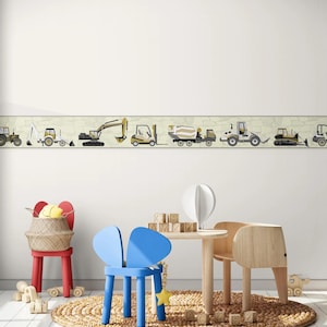 May include: A white wall with a border of construction vehicles in yellow, black, and gray. The vehicles include a bulldozer, excavator, forklift, cement mixer, and a dump truck. The border is above a playroom with a blue chair, a wooden table, and a woven rug.