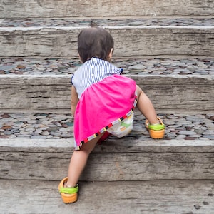May include: A young child in a pink and blue dress climbs up a set of stone steps. The steps are decorated with small, colorful stones.
