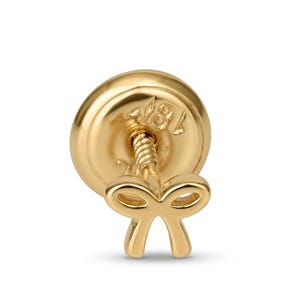 Puede incluir: Primer plano de un cierre de pendiente dorado con un diseño en forma de lazo. El cierre tiene un poste de rosca y una base redonda y plana. La base tiene el número "18" estampado.