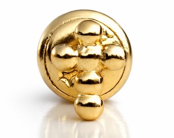May include: A circular gold-toned metal button featuring a raised cross design composed of small, smooth, spherical beads. The button has a polished, reflective surface and a rounded, domed profile, showcasing a metallic finish throughout the piece.