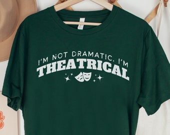 May include: Forest green t-shirt with white text that reads "I'm not dramatic, I'm theatrical" with two white masks and stars.