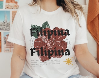 May include: White t-shirt with a red hibiscus flower graphic and the text "Filipina" repeated three times. The text is in a vintage style font. The shirt also features a small graphic of the Philippine flag.