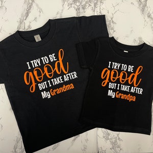 Könnte beinhalten: Zwei schwarze T-Shirts mit weißem Text und orangefarbener Schrift. Das größere Shirt sagt "Ich versuche, gut zu sein, aber ich bin meiner Oma nachempfunden". Das kleinere Shirt sagt "Ich versuche, gut zu sein, aber ich bin meinem Opa nachempfunden".
