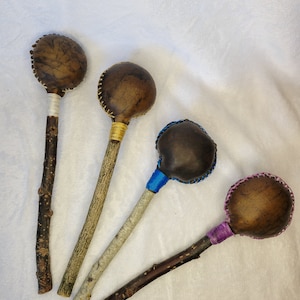 May include: Four handmade leather rattles with wooden handles. The rattles are brown with different colored stitching. The handles are natural wood.