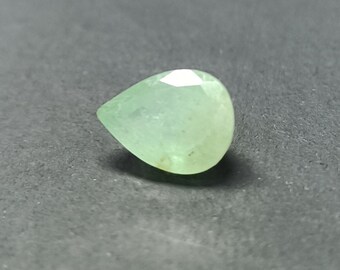 Puede incluir: Una piedra preciosa de forma de pera de color verde claro con facetas.
