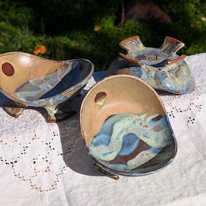 Può includere: Un set di tre tazze in ceramica con finitura opaca e macchiettata. Le tazze sono nei toni del crema, grigio chiaro e grigio scuro. Ogni tazza ha un design semplice e minimalista e un manico arrotondato.