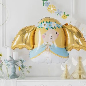 May include: A foil balloon shaped like an angel with blonde hair, a blue and white robe, and metallic gold wings. The angel figure features a floral crown of blue and white flowers, pink cheeks, and hands pressed together in a prayer position.