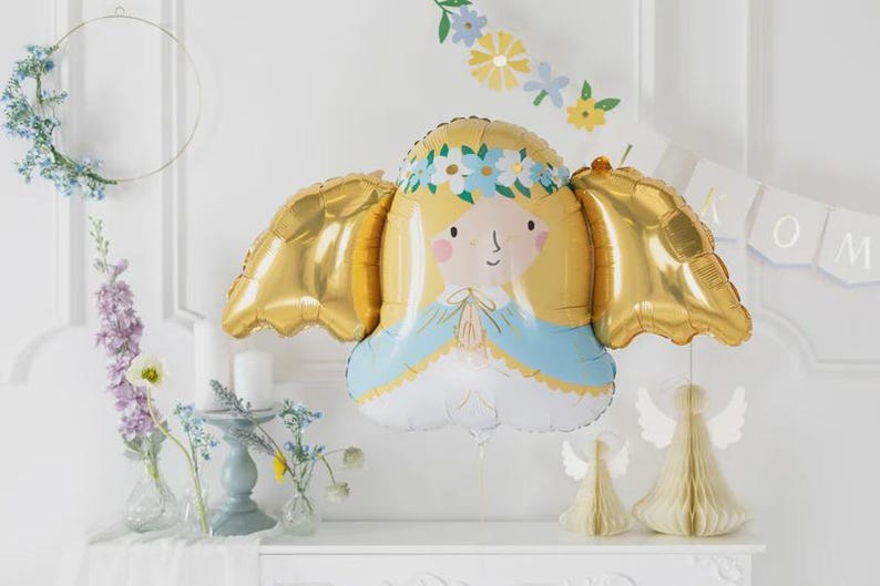 May include: A foil balloon shaped like an angel with blonde hair, a blue and white robe, and metallic gold wings. The angel figure features a floral crown of blue and white flowers, pink cheeks, and hands pressed together in a prayer position.