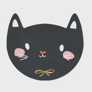 May include: A black cat-shaped paper napkin featuring white inner ears, white oval eyes, pink circular cheeks, white whiskers, a small orange nose, and a gold-colored bow illustration centered at the bottom of the cat's face.