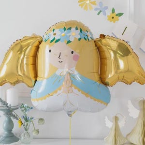 May include: A foil balloon shaped like a stylised angel with blonde hair, a blue and white robe, and large gold wings. The figure has a floral crown, pink cheeks, and hands pressed together in a prayer position, attached to a thin gold string.