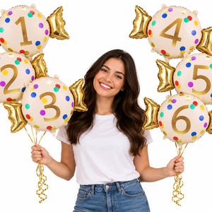 May include: A set of six cream-colored foil balloons shaped like wrapped candies, each featuring a large gold number from one to six and colorful polka dots. The balloons have metallic gold twisted ends and are attached to gold ribbons.