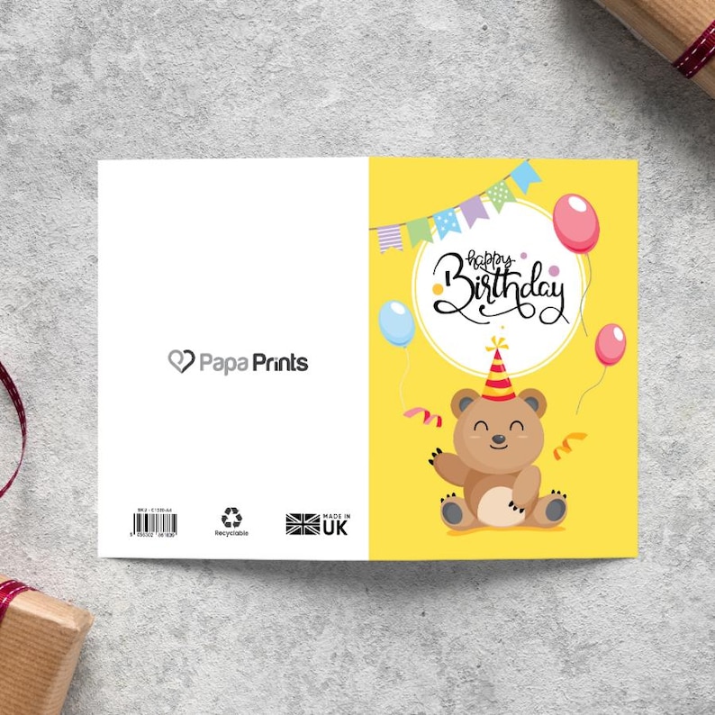 May include: A yellow birthday card with a cartoon bear wearing a party hat and holding a streamer. The card says "Happy Birthday" in a white circle with colorful flags hanging above.