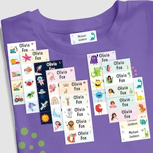 May include: A set of colourful iron-on labels with various cartoon images and the name "Olivia Fox" printed on each label. The labels are arranged on a purple t-shirt with white polka dots. There is also a label with the name "Michael Jackson" on the shirt.