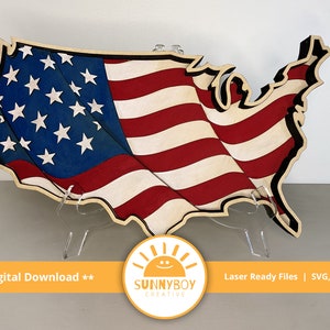 Könnte beinhalten: Ein Holzausschnitt der Vereinigten Staaten von Amerika mit einem wellenförmigen amerikanischen Flaggenmuster. Der Ausschnitt steht auf einem Ständer und ist bereit für Bastelarbeiten.
