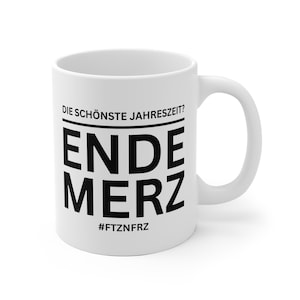 Könnte beinhalten: Weiße Keramik-Tasse mit schwarzem Grafikdesign. Der Text auf der Tasse lautet "DIE SCHÖNSTE JAHRESZEIT? ENDE MERZ" mit dem Hashtag "#FTZNFRZ" darunter. Die Tasse hat einen gebogenen Griff.