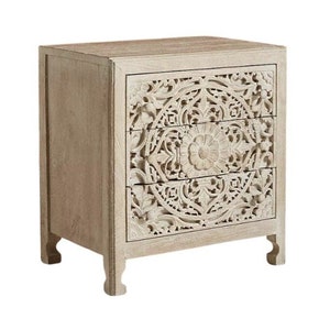 May include: A white wooden chest of drawers with three drawers featuring intricate carved floral designs.