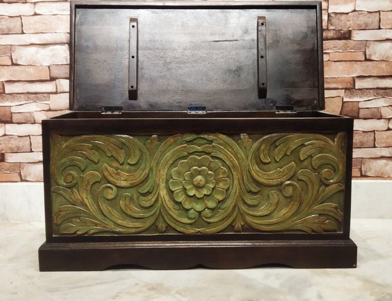 May include: A wooden storage chest with a carved floral design in green and brown. The lid is open, revealing the interior of the chest.