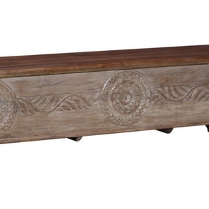 May include: A carved wooden storage chest with a light brown finish and a dark brown top. The chest has intricate floral designs and sits on four turned legs.