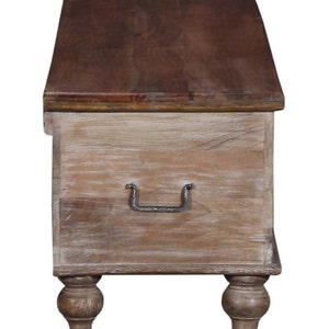 May include: A whitewashed wooden storage chest with a dark brown wood top and a metal handle. The chest has four turned legs.