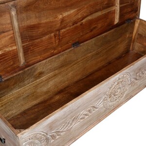 May include: A wooden storage chest with a carved design on the front. The lid is open, revealing the empty interior. The chest is made of light wood with a whitewash finish.