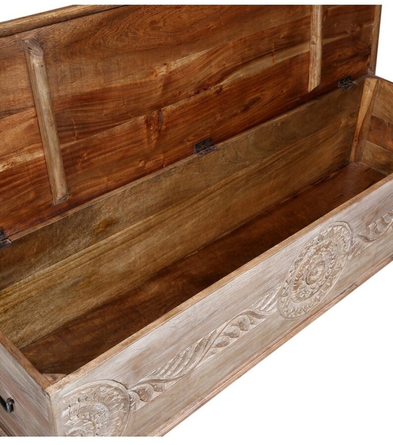 May include: A wooden storage chest with a carved design on the front. The lid is open, revealing the empty interior. The chest is made of light wood with a whitewash finish.