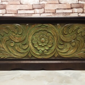 May include: A wooden storage box with a carved floral design in green and brown. The box has a hinged lid and a decorative base.