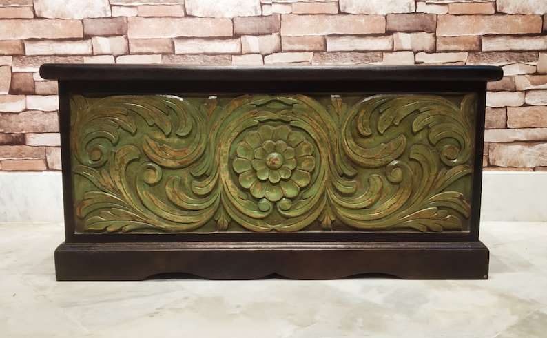 May include: A wooden storage box with a carved floral design in green and brown. The box has a hinged lid and a decorative base.