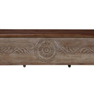 May include: A large, rectangular wooden storage chest with intricate carvings. The chest has a light brown finish and features a decorative floral design. It has four turned legs.