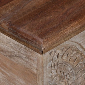 May include: A wooden storage box with a carved design on the front. The top of the box is a darker wood and has a smooth finish.