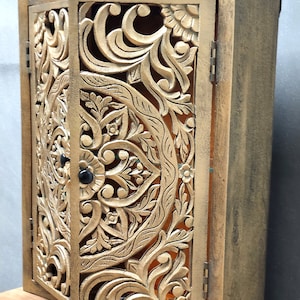May include: A wooden cabinet with intricate carved floral designs in a gold finish. The cabinet has two doors that are open, revealing the interior.