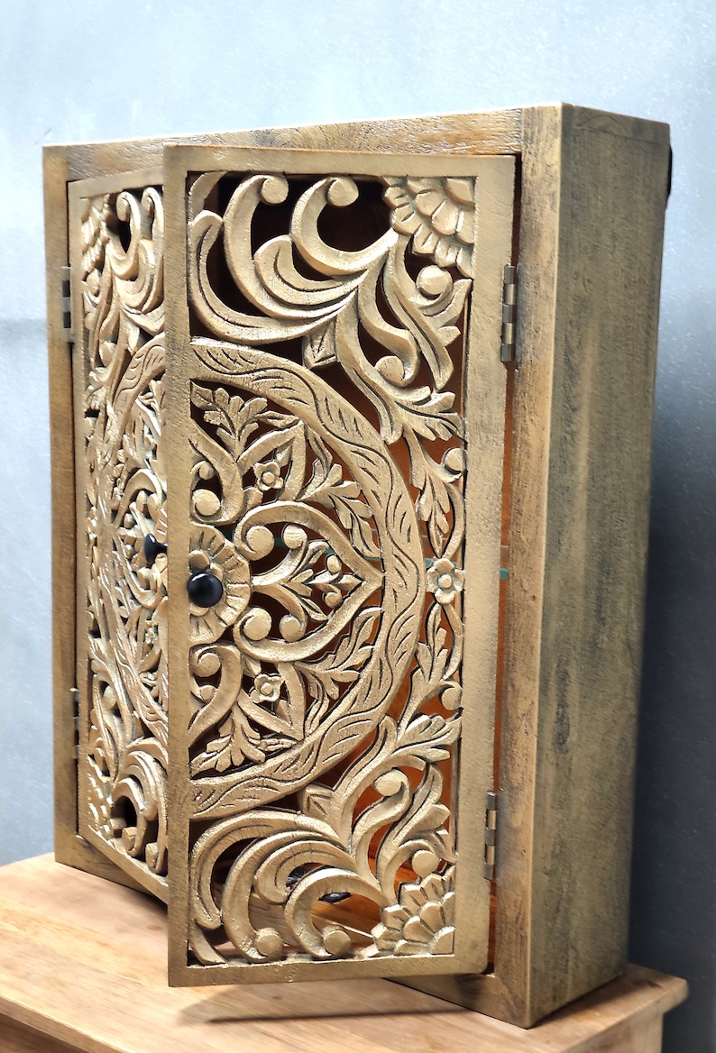 May include: A wooden cabinet with intricate carved floral designs in a gold finish. The cabinet has two doors that are open, revealing the interior.