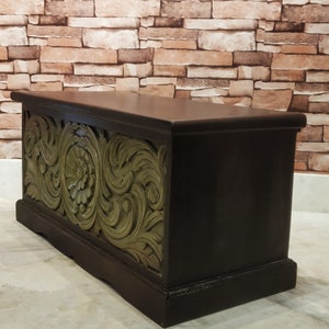 May include: A dark brown wooden storage chest with intricate green carved floral designs. The chest has a rectangular shape and a slightly raised lid.