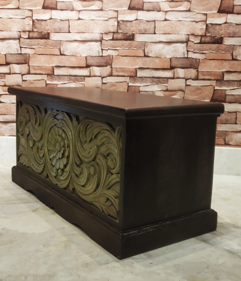 May include: A dark brown wooden storage chest with intricate green carved floral designs. The chest has a rectangular shape and a slightly raised lid.