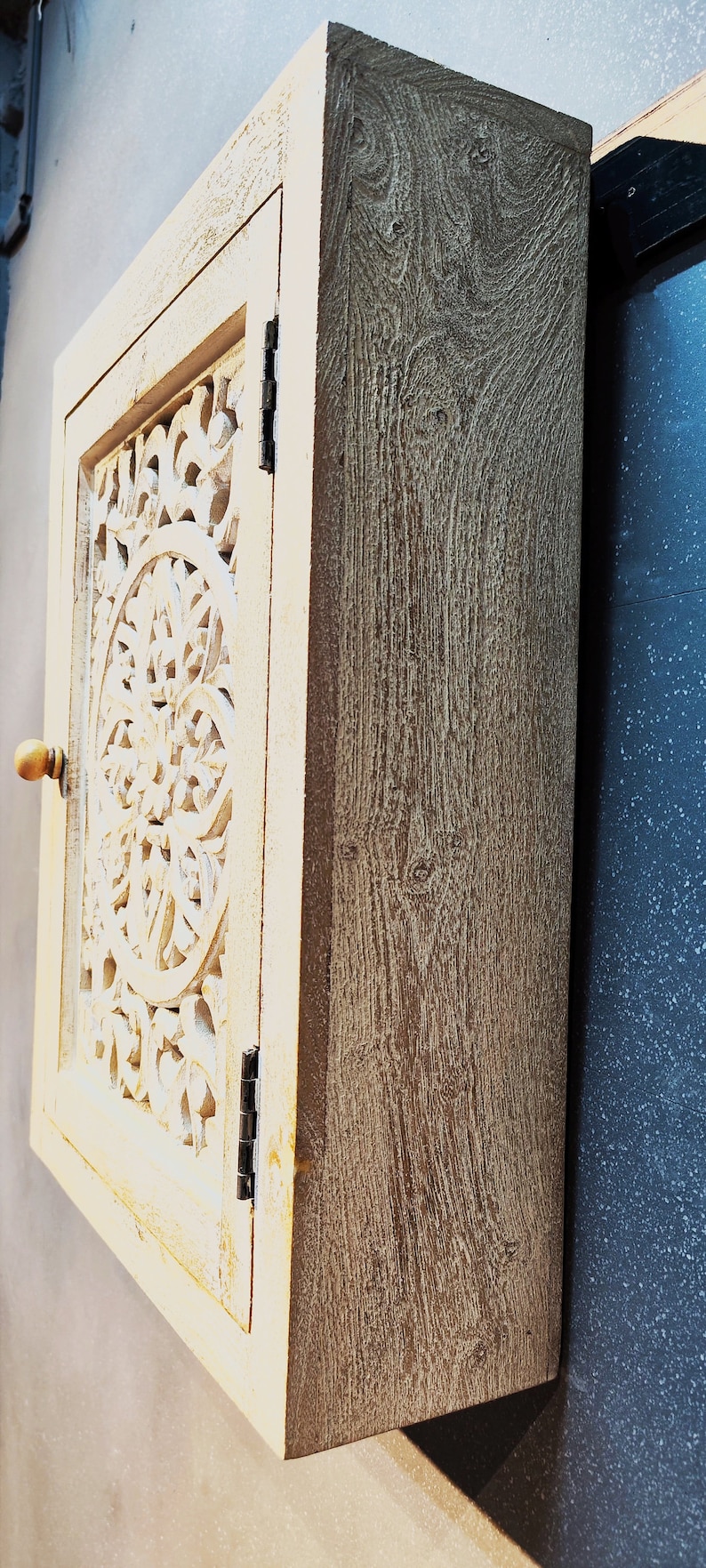 May include: A white wooden cabinet with a carved floral design on the door. The cabinet has a light brown finish and a simple knob.