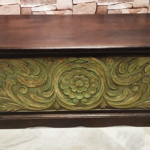 May include: A wooden storage chest with a dark brown finish and intricate green floral carvings. The chest has a hinged lid and a decorative base.